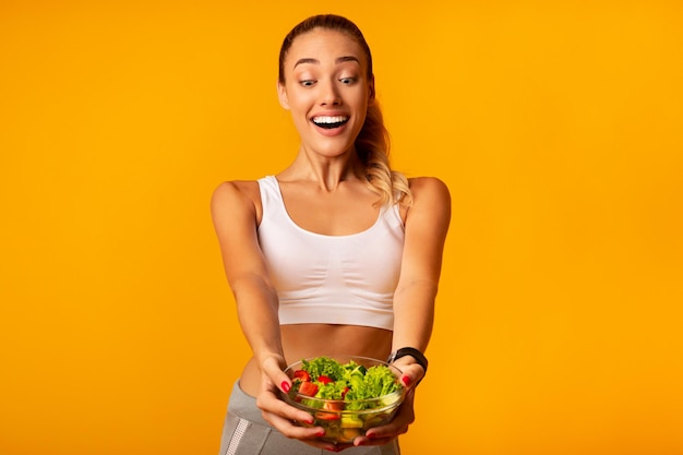 Excited Slim Woman Holding Vegetable Salad Standing On Yellow Background