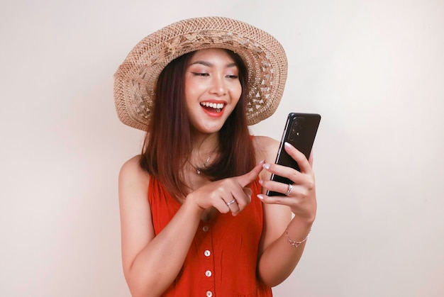 Excited and smiling young Asian woman pointing finger at smartphone in her hand