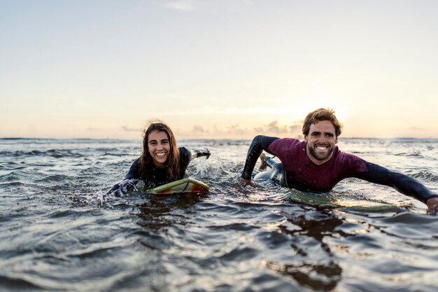 Photo excited surfer couple is swimming with boards and rushing to catch the waves