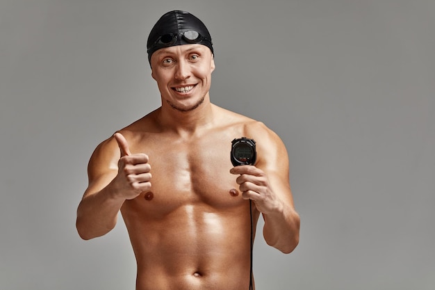 Excited swimer with stopwatch standing on gray background. New record. Motivation, advertising banner, place for text.