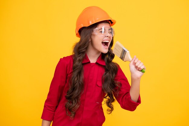 Excited teenager builder expert in helmet on construction site Teen girl painter with painting brush tool or paint roller Child on repairing work Renovation concept