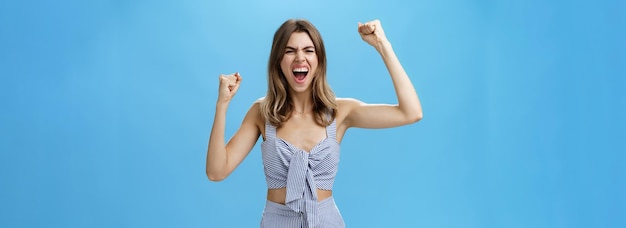 Excited and thrilled overwhelmed attractive woman in matching stylish clothes becoming fan of football standing on stadium yelling to cheer team raising clenched fists in rage and victory gesture