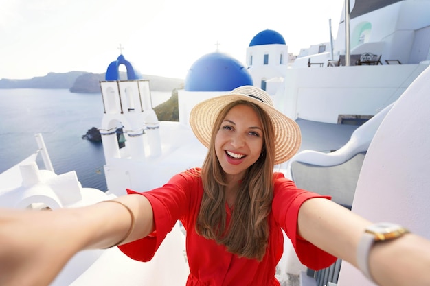 Excited traveler girl taking selfie photo in Santorini on sunset Young woman having fun in Oia pictureque village in Greece