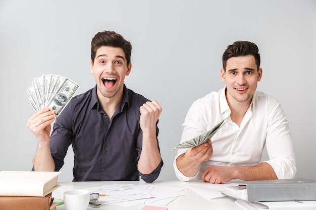 Excited two young business men colleagues holding money.