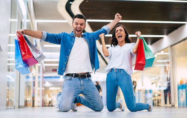 Excited winning couple in love or family with paper bags in hands while are shouting during shopping in the mall