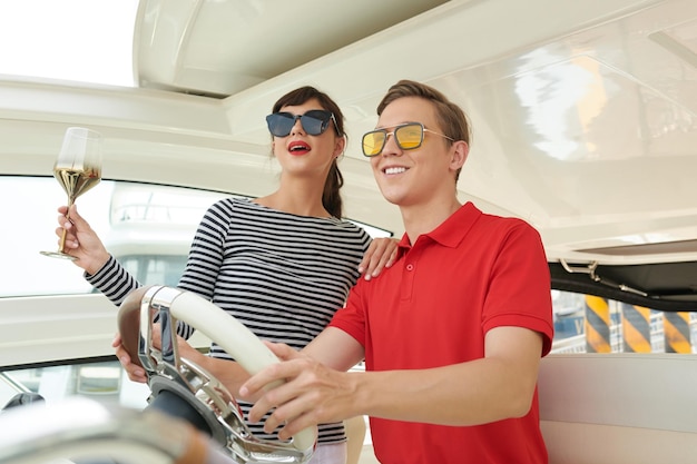 Excited woman drinking glass of wine when her boyfriend navigating sail boat or yacht floating in sea