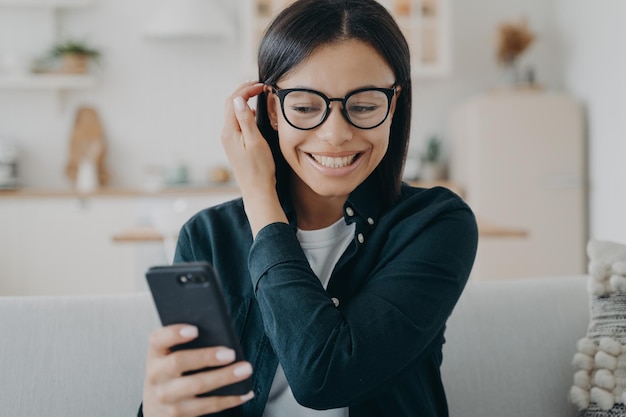 Excited woman holding smartphone got good news message in social networks sitting on couch at home