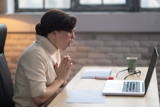 An excited woman sitting at the laptop and looking surprised