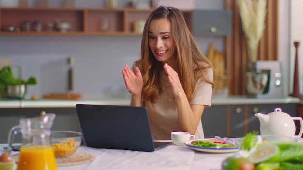 Excited woman talking with friend online on laptop computer at modern kitchen Portrait of happy lady gesturing on web camera at home Emotional girl having online conversation on laptop at kitchen