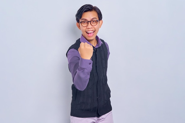 Excited young Asian man in casual shirt and vest celebrating victory or success with raised fists up isolated on white background People lifestyle concept