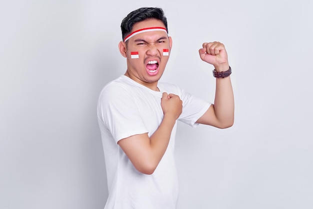 Excited young Asian man clenched fist showing excitement during celebrating indonesian independence day on 17 august isolated on white background