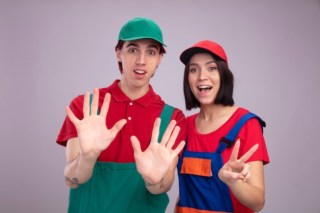 Excited young couple in construction worker uniform and cap guy showing ten with hands girl showing two with hand 