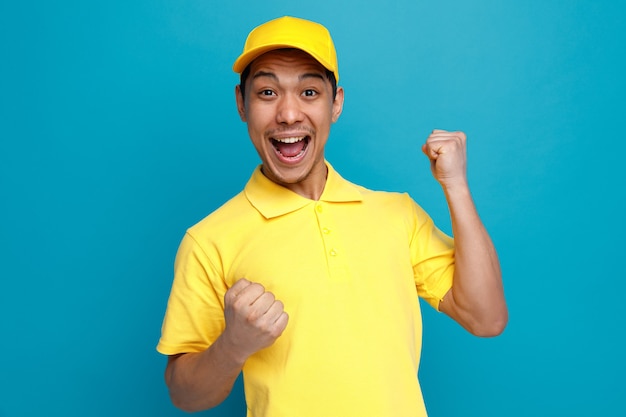 Excited young delivery man wearing uniform and cap doing yes gesture 