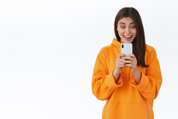 Excited young girl attend cool concert record video for her vlog, stream music festival online via social media, holding smartphone and looking at display with amazed happy face to take shot