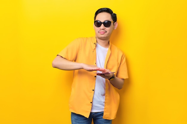 Excited young handsome Asian man throwing banknotes isolated on yellow background