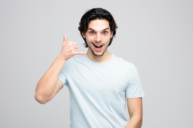 excited young handsome man looking at camera showing call gesture isolated on white background