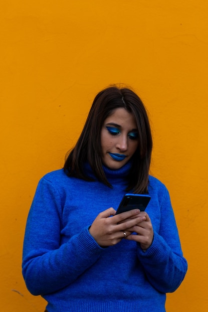 Excited young lady with blue clothes chatting with her mobile social network message vertical portrait on orange background