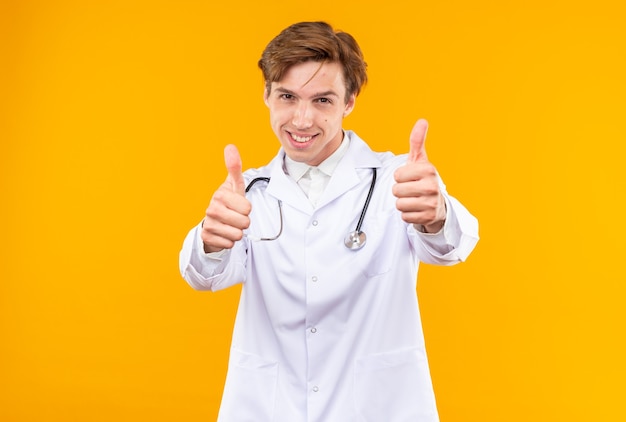 Excited young male doctor wearing medical robe with stethoscope showing thumb up