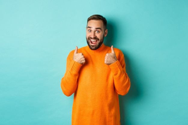 Excited young man with beard, showing thumbs up in approval, praise or recommend, standing over