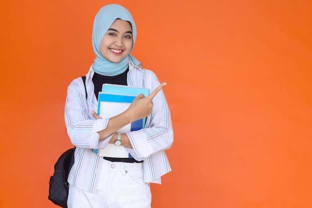 Excited young muslim woman student with backpack holding books and pointing finger up