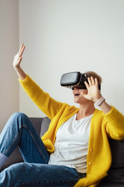 Excited young sitting on the sofa and using virtual reality headset at home