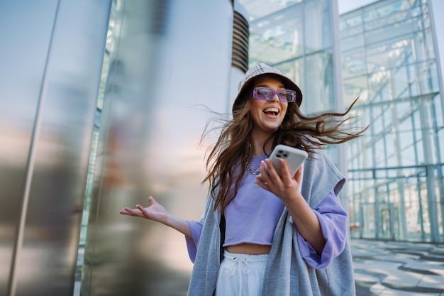 Excited young smiling woman holding and using mobile phone cool stylish girl at outside high quality