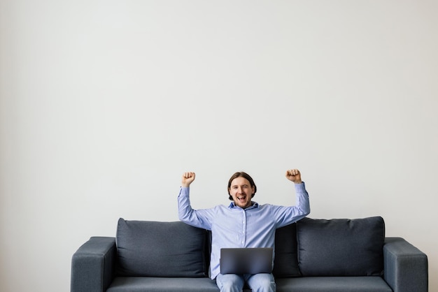 Excited young win man using laptop computer while sitting on a sofa at home