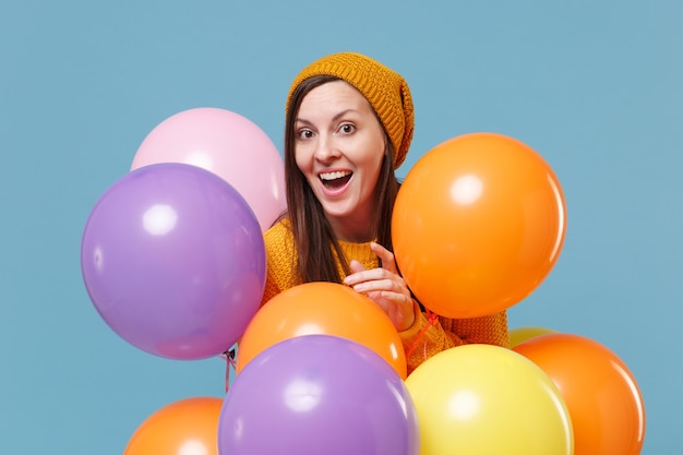 Excited young woman girl in sweater hat posing isolated on blue wall  portrait. Birthday holiday party, people emotions concept.  Celebrating hold colorful air balloons.