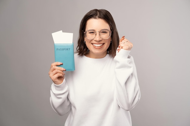 Excited young woman is holding a blue passport near her face while smiling