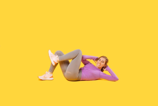 Excited young woman is making some abdomen crunches over yellow background