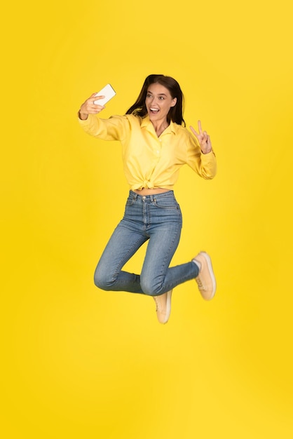 Excited young woman jumping up and taking selfie