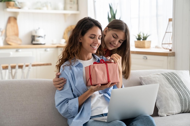 Excited young woman mother getting wrapped gift box present from daughter while sitting on sofa