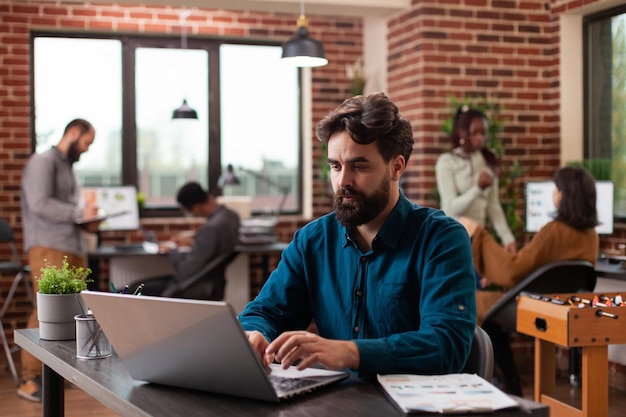 Executive manager analyzing marketing statistics working at business project in brick wall startup office. Freelancer man typing company turnover on laptop computer brainstorming ideas