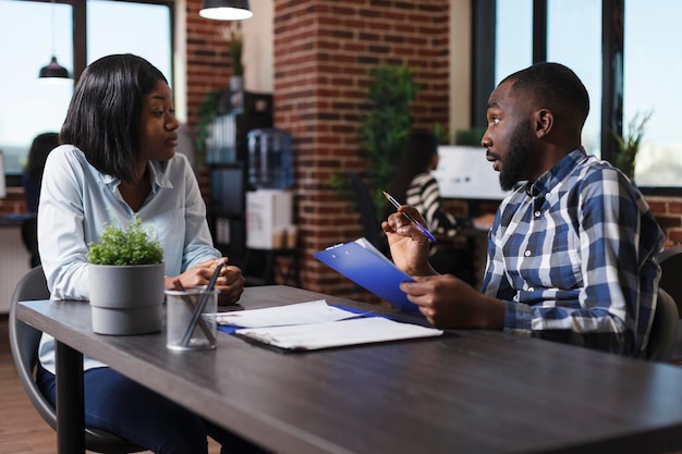 Executive manager having candidate CV resume while discussing about job description and salary offer. Job applicant sitting at desk in office while listening to employer talking about work policy