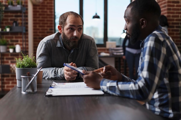 Executive manager interviewing confident man while reviewing CV and asking questions about work experience in field. African american businessman presenting applicant job and salary offer.