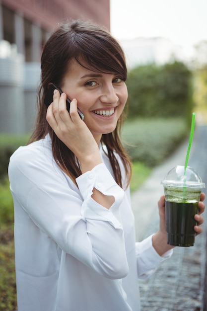 Executive talking on mobile phone while having juice on road