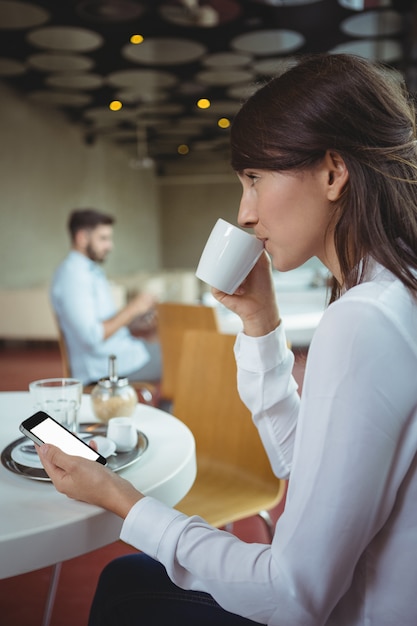 Executive using mobile phone while having coffee in cafeteria