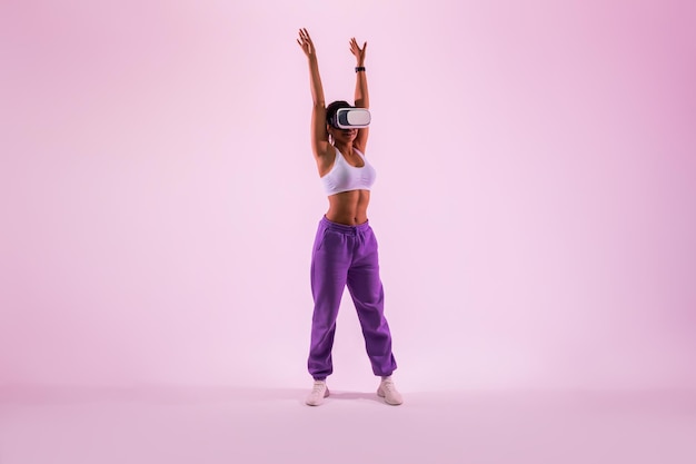 Exercising beyond reality Fit black woman training in vr headset doing exercise in metaverse pink neon background