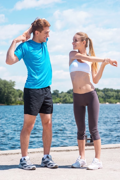 Exercising together is fun. Beautiful young woman and man doing stretching exercises together while standing outdoors