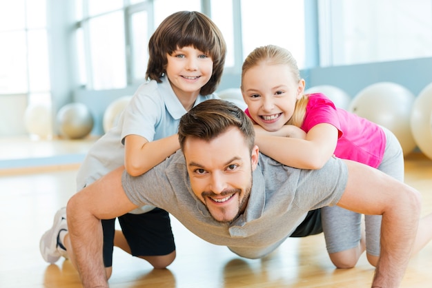 Exercising with father. Happy little children bonding to their father doing push-ups in sports club