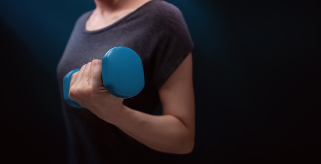 Exercising Workout with Dumbbell Sport and Recreation Concept Closeup of Woman with blue Dumbbell in Dark Room at Home or Gym