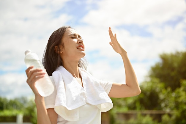 An exhausted Asian woman is fighting the heat wave while running in a park on a sunny summer day