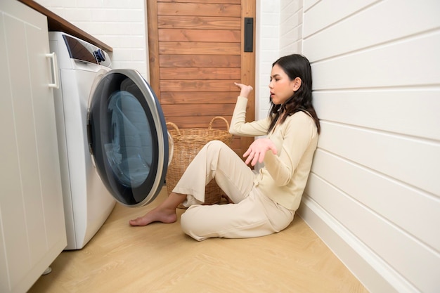 Exhausted Asian young woman with dirty clothes doing laundry in home