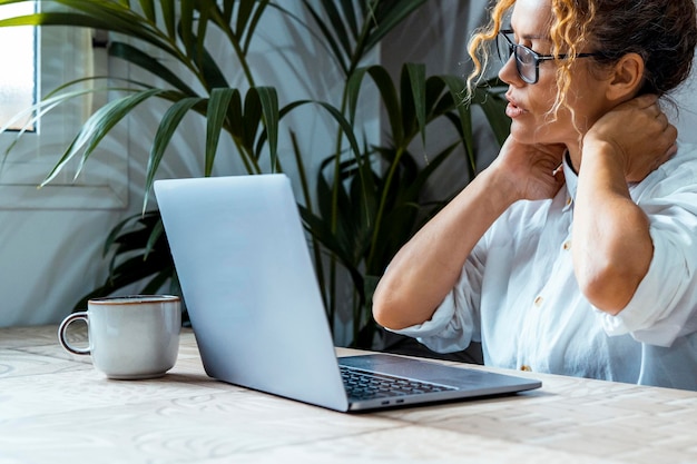 Exhausted business woman massaging her back neck in front of a laptop computer. Online smart working. Bad posture sitting on the desk and using notebook. Tired female people overwork. Overtime working