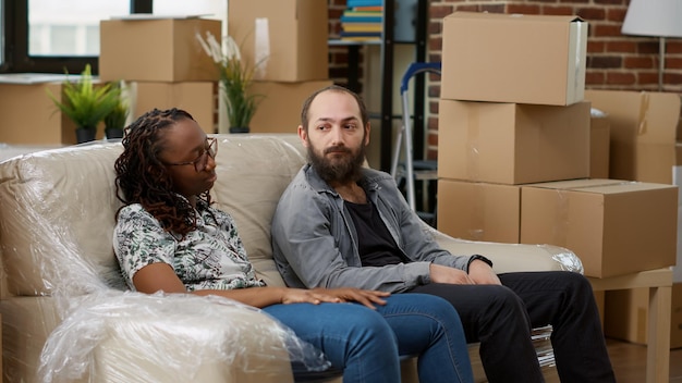 Exhausted life partners taking break after moving boxes in apartment, relaxing on couch and celebrating home investment. Feeling tired about decorating new real estate property.