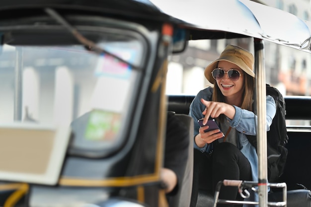 Exited caucasian woman tourist with sunglasses sitting in back seat of Tuk Tuk public transport in Thailand