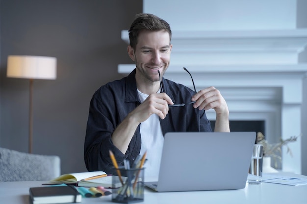 Exited german man freelancer looking on laptop with happy smile while holding glasses in hands