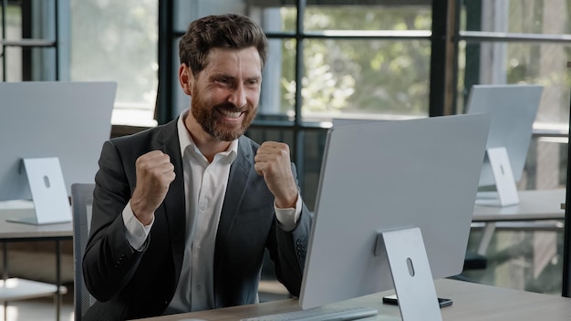 Exited happy caucasian bearded businessman in office looking at computer with emotion winner