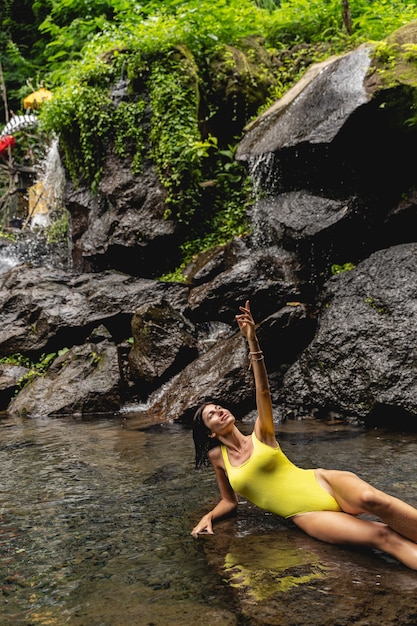 Exotic island. Pleased brunette looking upwards at sky while leaning on stone in water