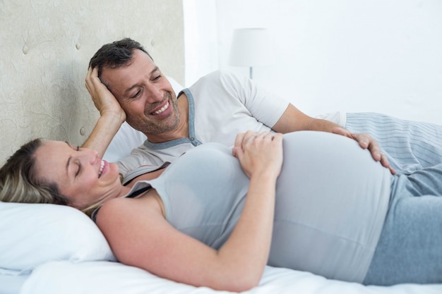 Expecting couple lying on bed and chatting in their bedroom